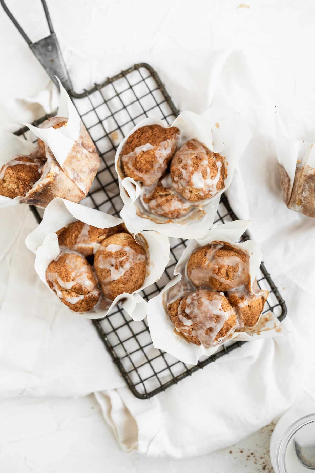 Muffins with white paper liners scattered on a cooling rack with glaze.