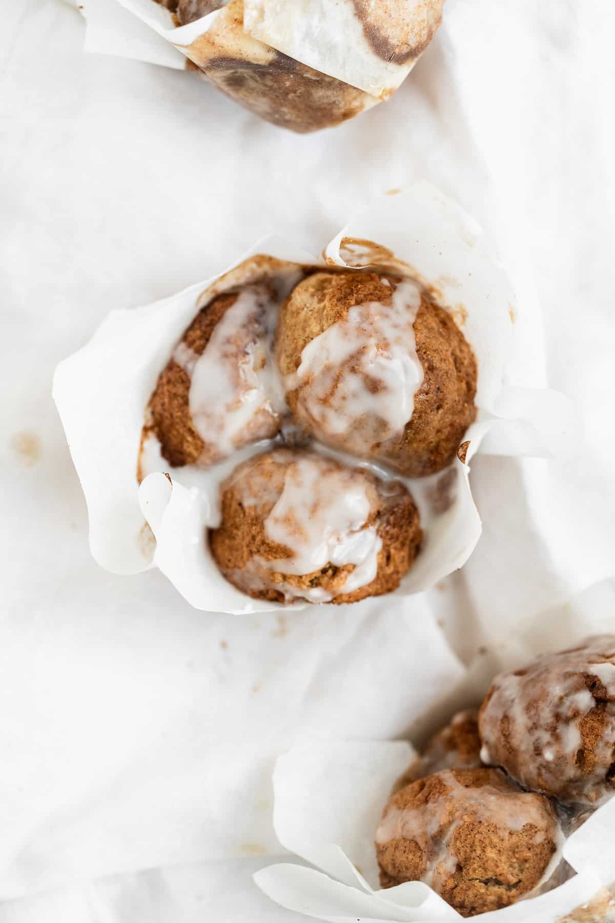 Up close view of a tan muffin with a white paper liner and glaze dripping off the sides.