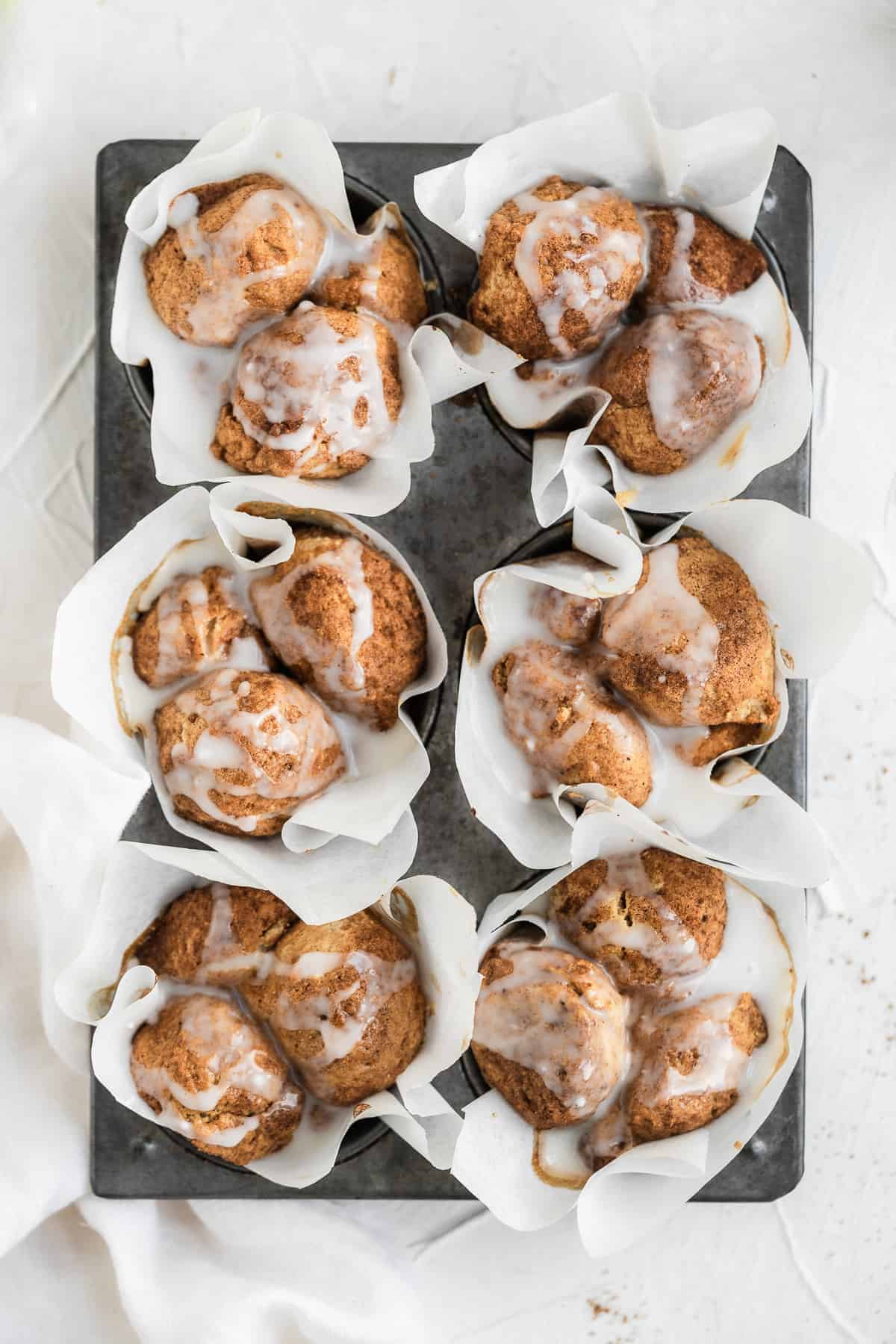 Six muffins in a grey tin with white paper liners and a white glaze.