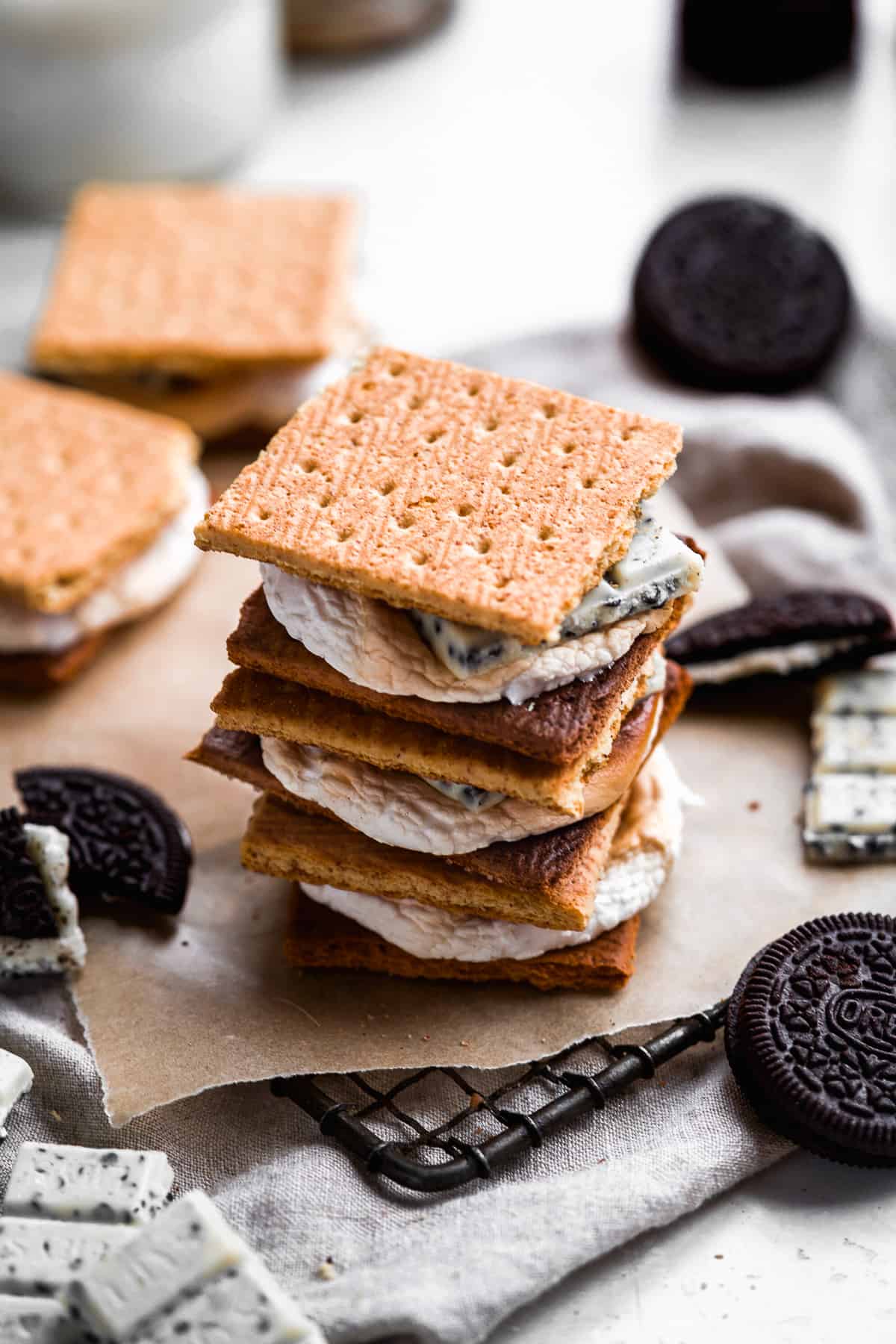 View from above of a stack of three Cookies and Cream Gluten-free S'mores sitting on parchment paper on a metal cooling rack.  Oreo cookies are sitting nearby.  