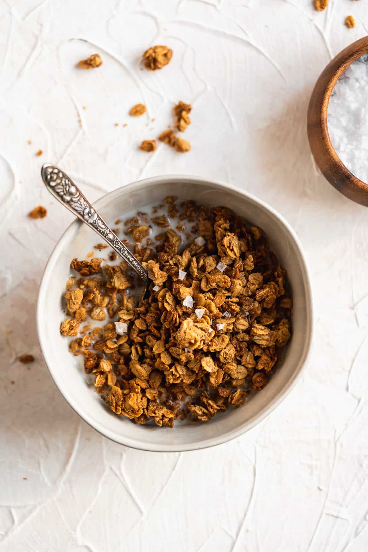 An overhead photo of a bowl of Maple Sea Salt Nut-free Granola topped with milk ready to be enjoyed.  A silver spoon is in the bowl.  
