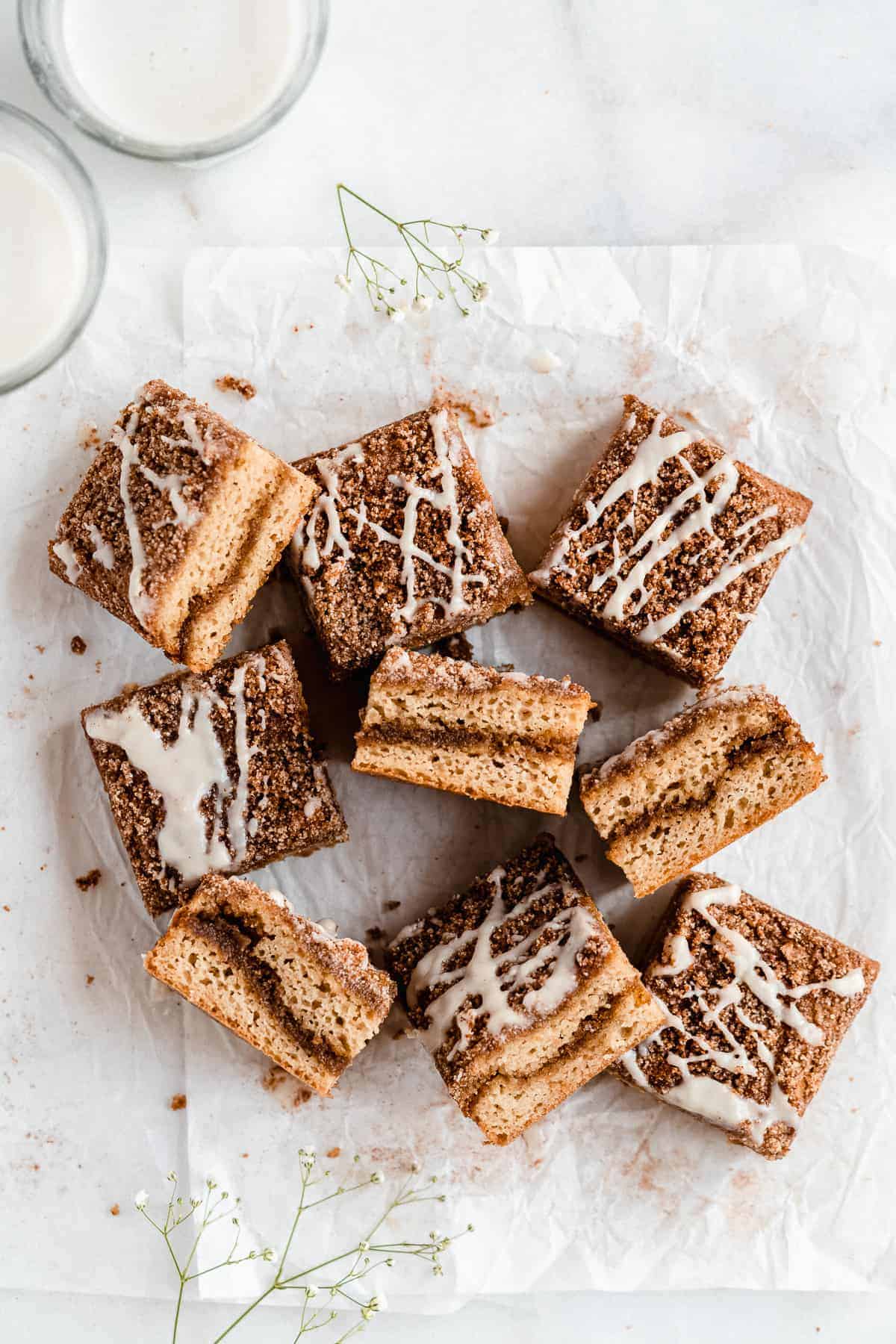 Overhead photo of freshly baked Paleo Almond Flour Coffee Cake that has been cut into squares and arranged on parchment paper on a marble slab. Two glasses of milk can be seen in the background.