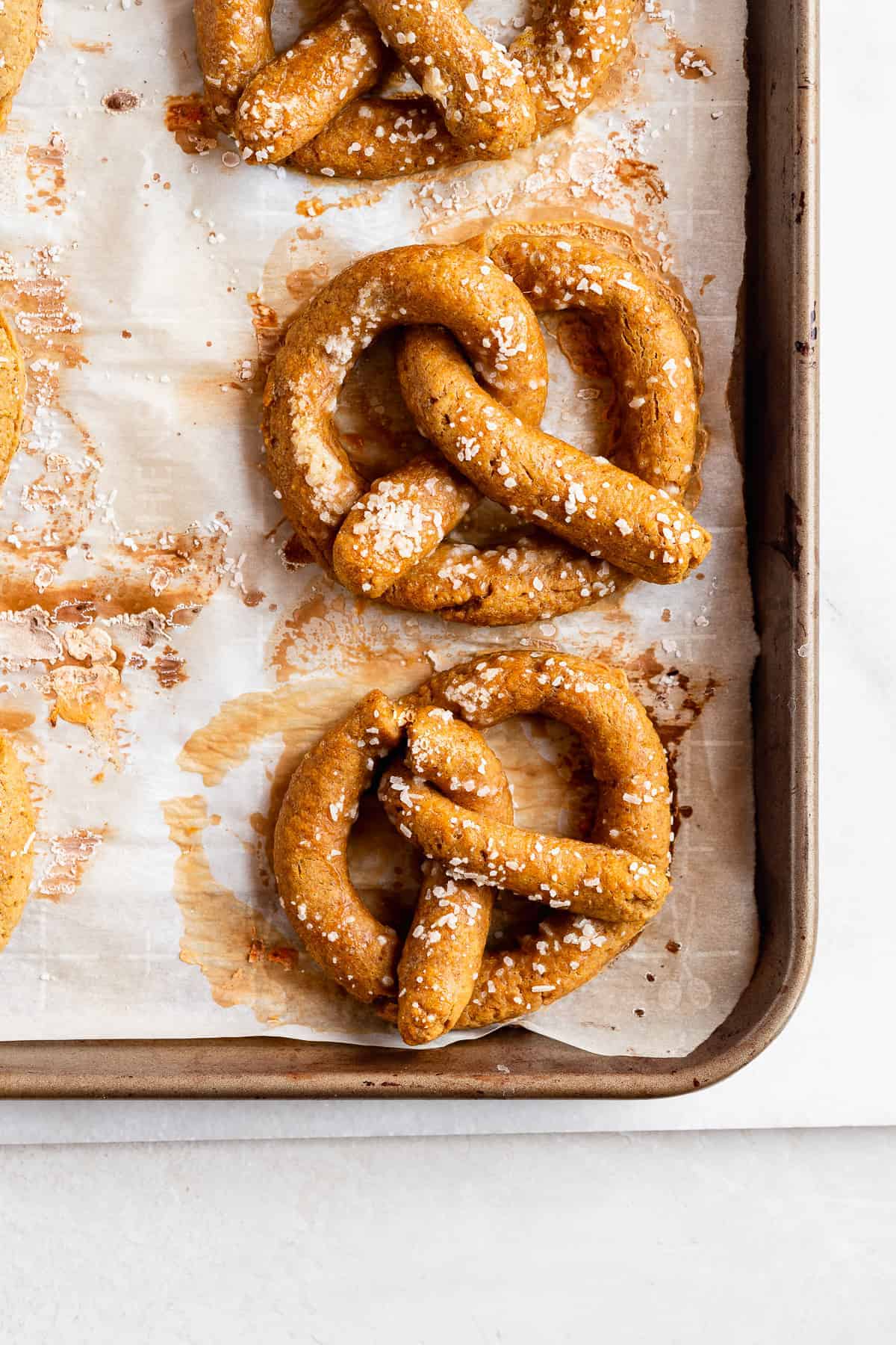 Overhead photo of a baking sheet with parchment paper and several Gluten-free Soft Pretzels hot out of the oven.