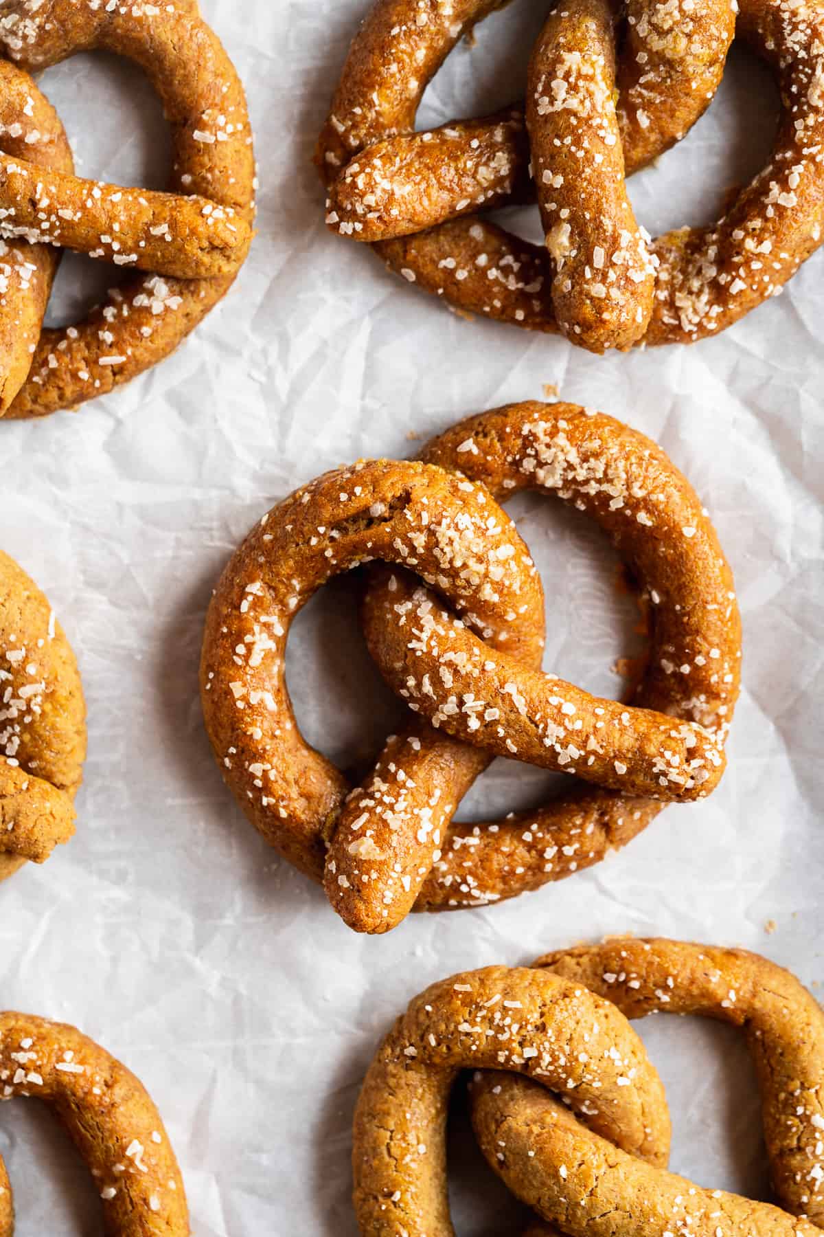 Close up overhead photo of several freshly baked Gluten-free Soft Pretzels cooling on parchment paper.  
