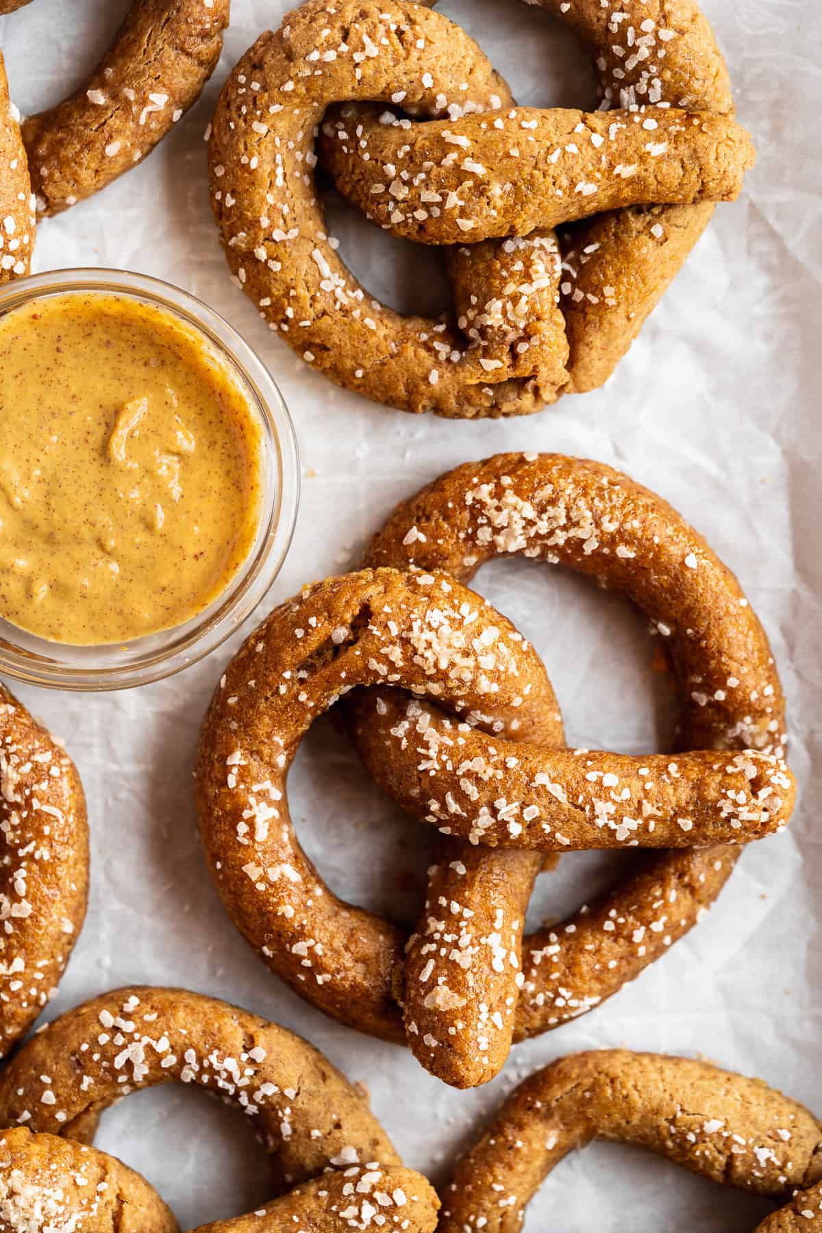 Close up photo of several Gluten-free Soft Pretzels sitting on white parchment paper.  A small bowl of dipping sauce is sitting nearby.  