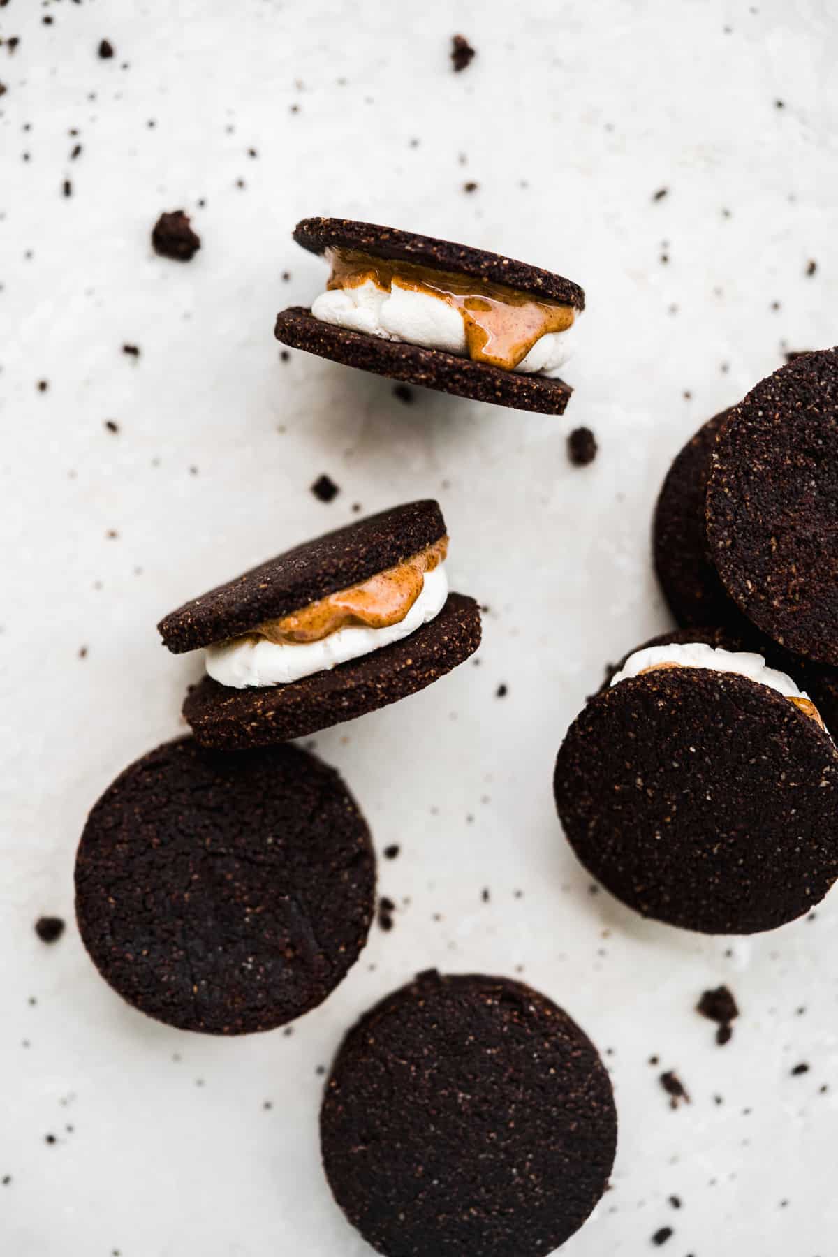 Close up photo of several Vegan Almond Butter Marshmallow Oreo Cookies showing a side view to reveal all the layers.  Additional cookies are sitting nearby.  