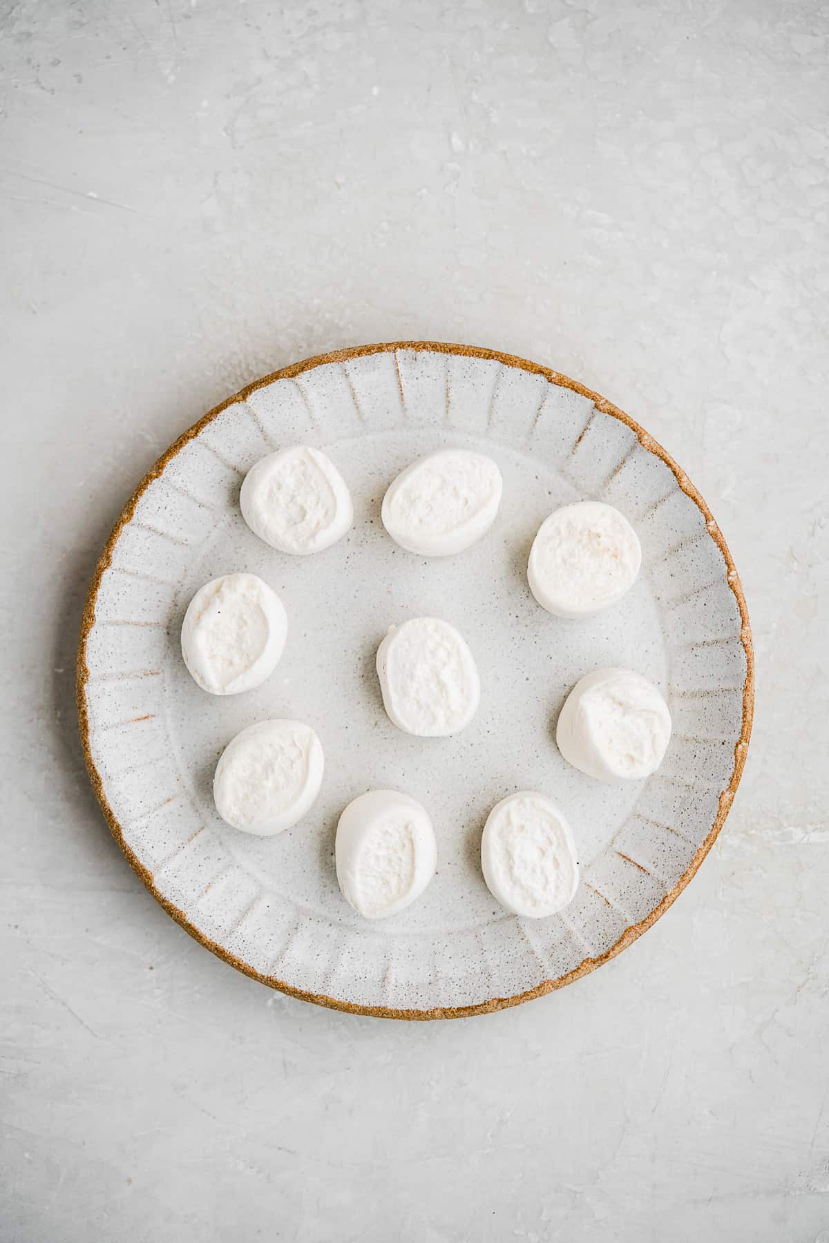 Marshmallows spread out on a plate on a white surface.