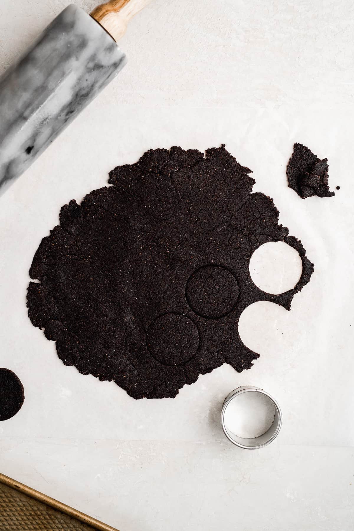 Chocolate cookie dough rolled out on a white surface with circles cut out.