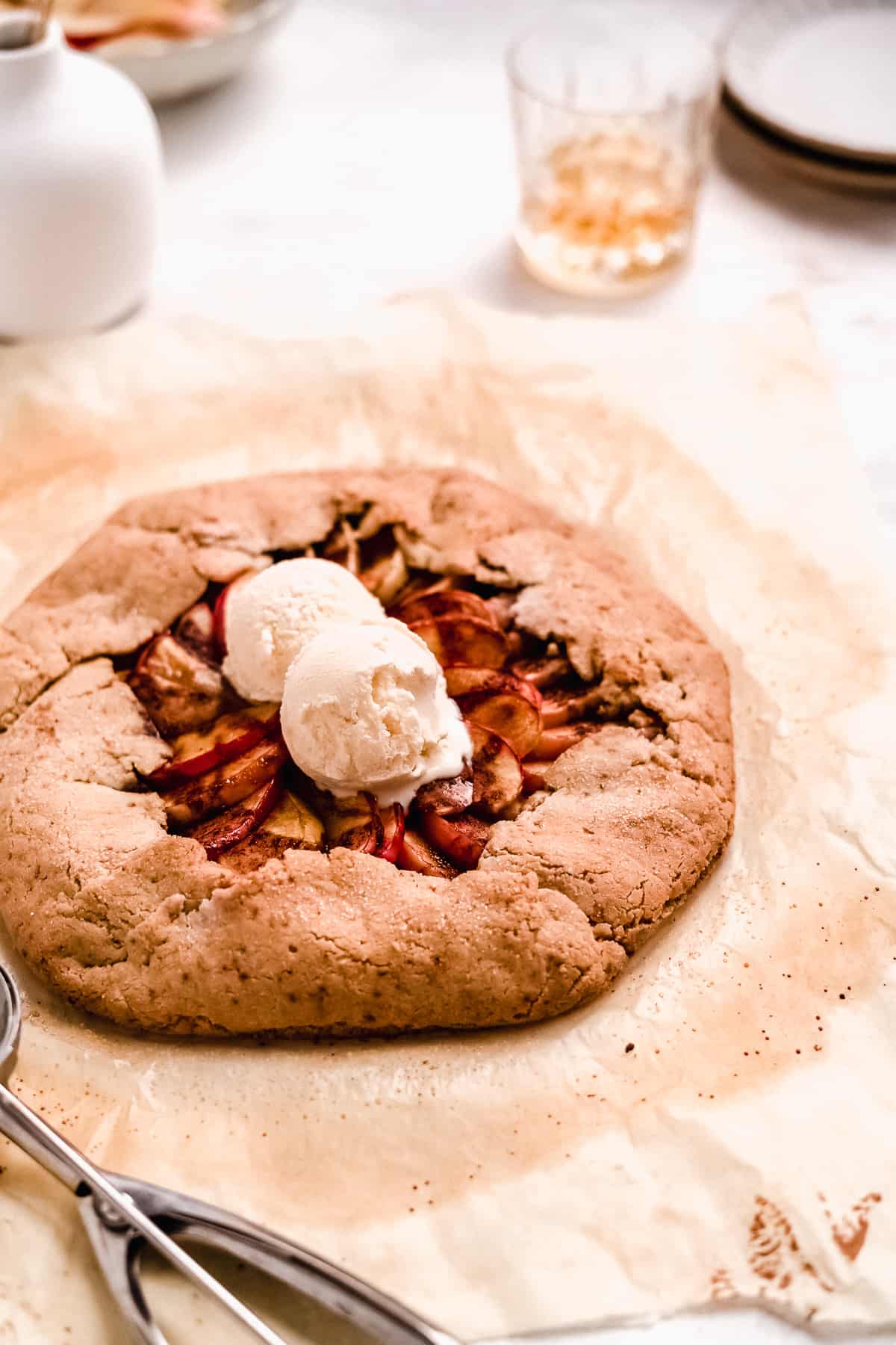 Overhead view of baked Bourbon Apple Galette on parchment paper with two scoops of vanilla ice cream.  