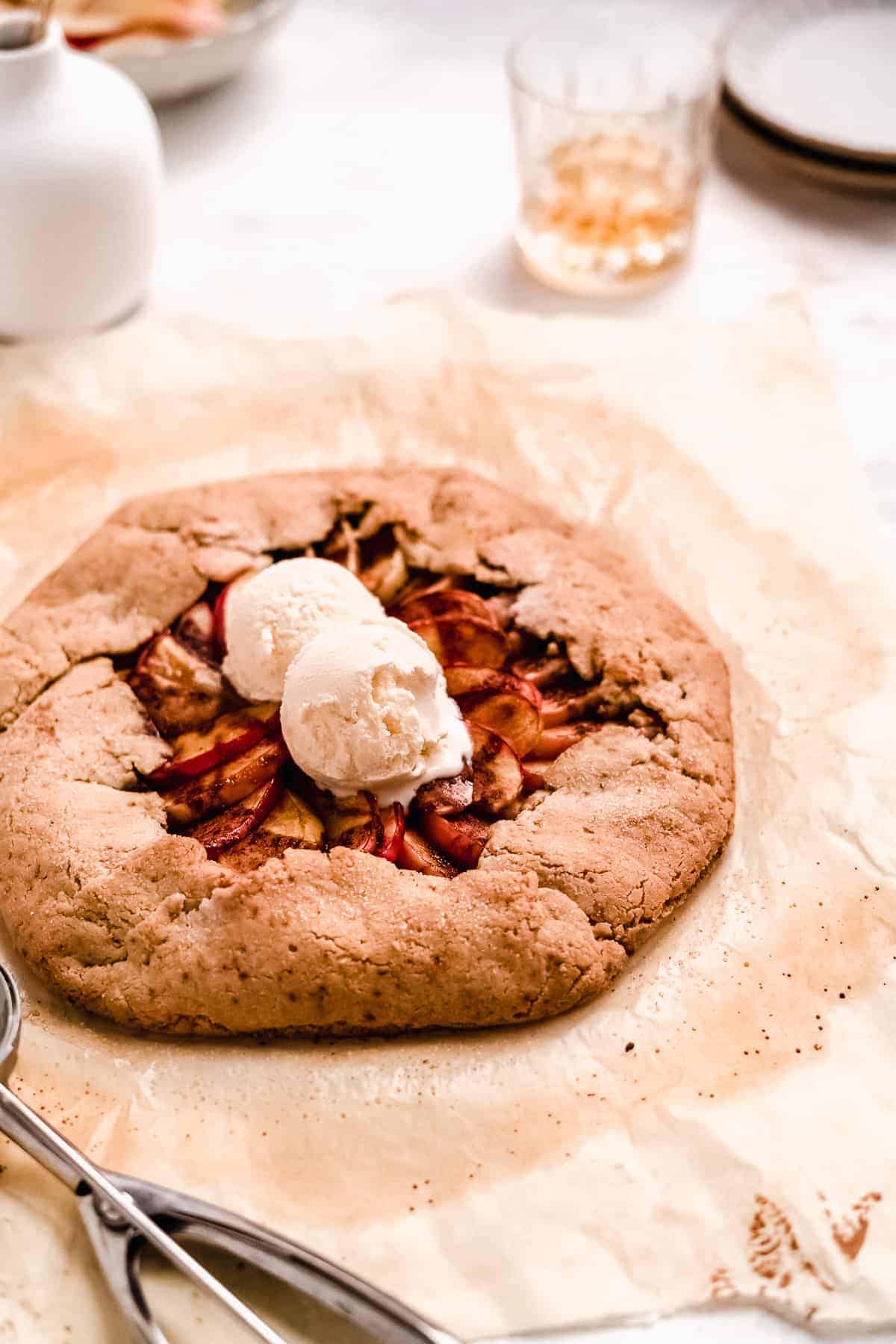 Overhead view of baked Bourbon Apple Galette on parchment paper with two scoops of vanilla ice cream.