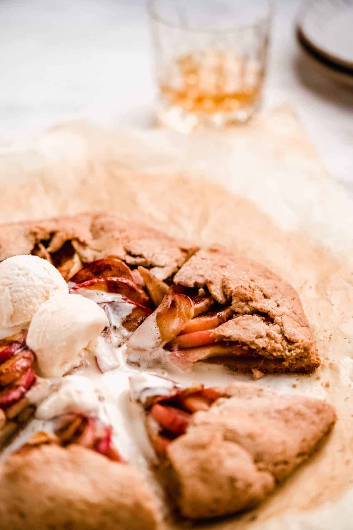 Close up overhead view of baked Bourbon Apple Galette with two scoops of vanilla ice cream melting on top.  Galette has been cut into pizza like triangle pieces to be served and enjoyed.  