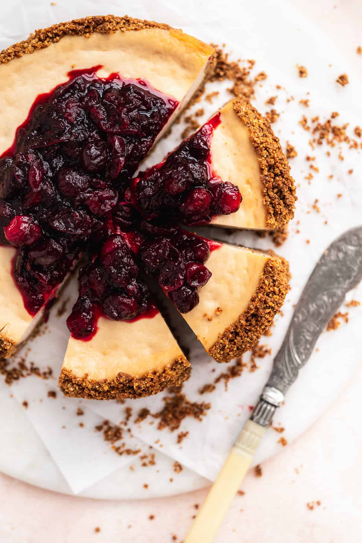 Overhead photo of the Vegan Baked Cranberry Cheesecake with Graham Cracker Crust with 3 slices cut and separated from the whole cake.  Silver pearl handled knife lays nearby.  
