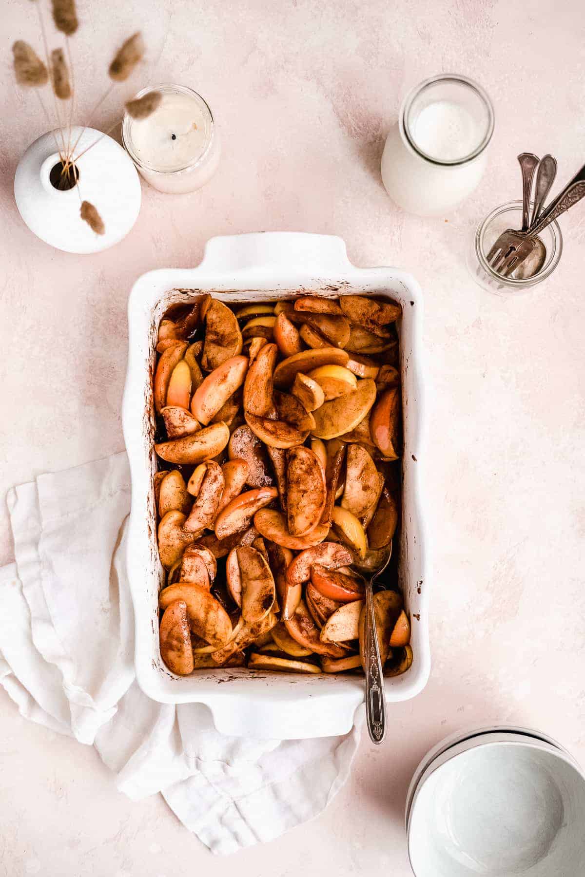 Overhead photo of rectangular white baking dish with the freshly baked Cinnamon Apples right out of the oven. Forks and spoons are sitting nearby.