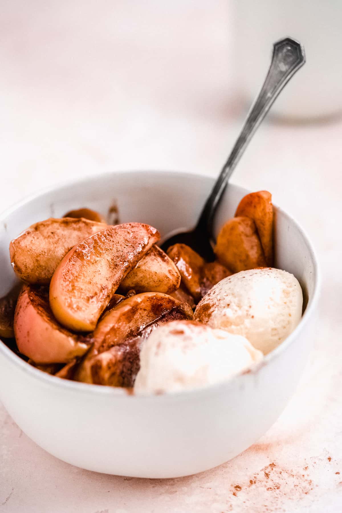 White bowl with freshly baked Cinnamon Apples served a la mode with two scoops of vanilla ice cream.  