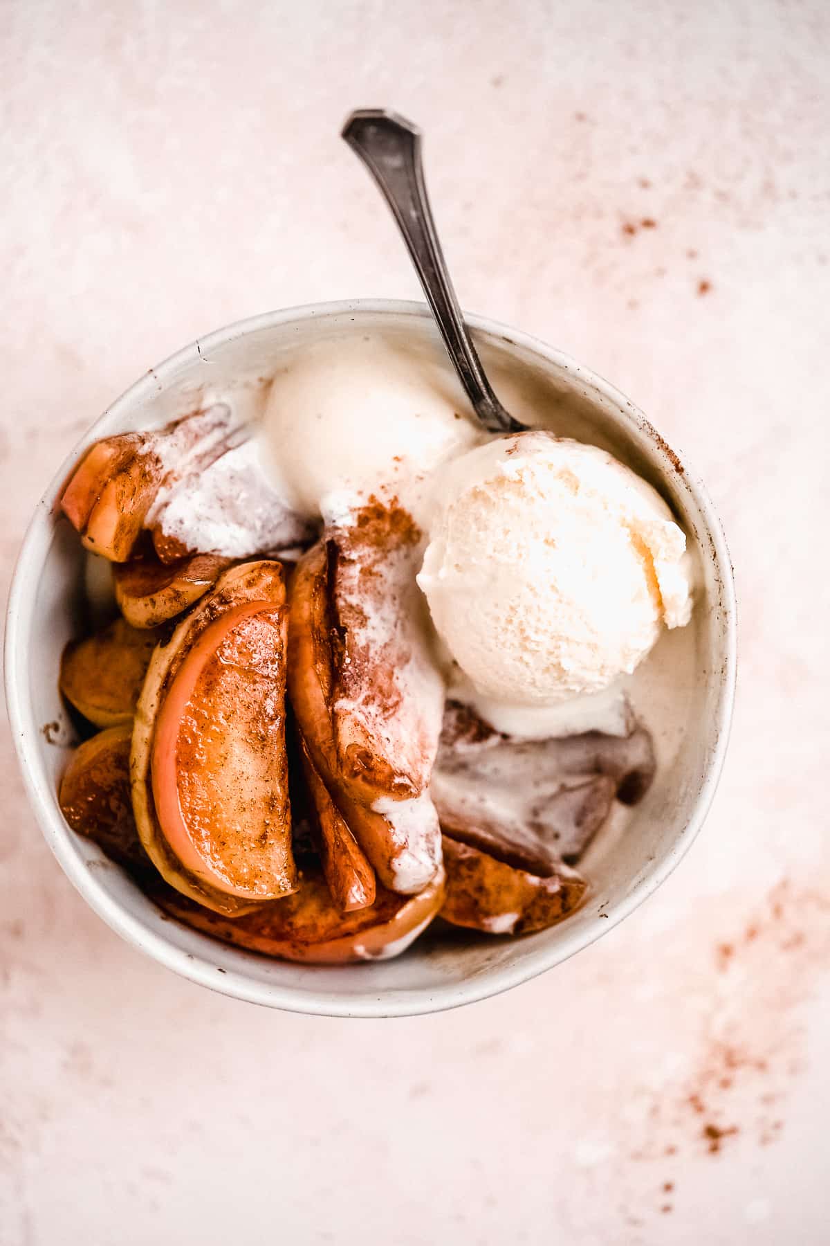 Overhead photo of Easy Baked Cinnamon Apples in a bowl with a silver spoon and served a la mode with a scoop of vanilla ice cream.