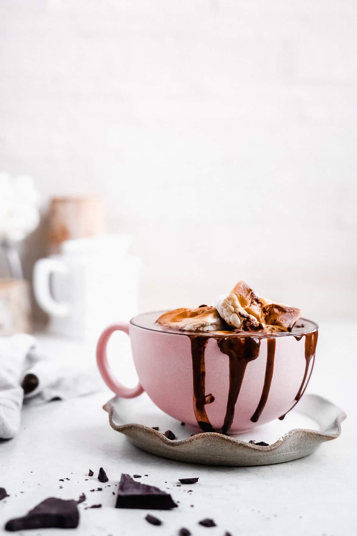 Pink mug overflowing with hot chocolate with marshmallows on top.