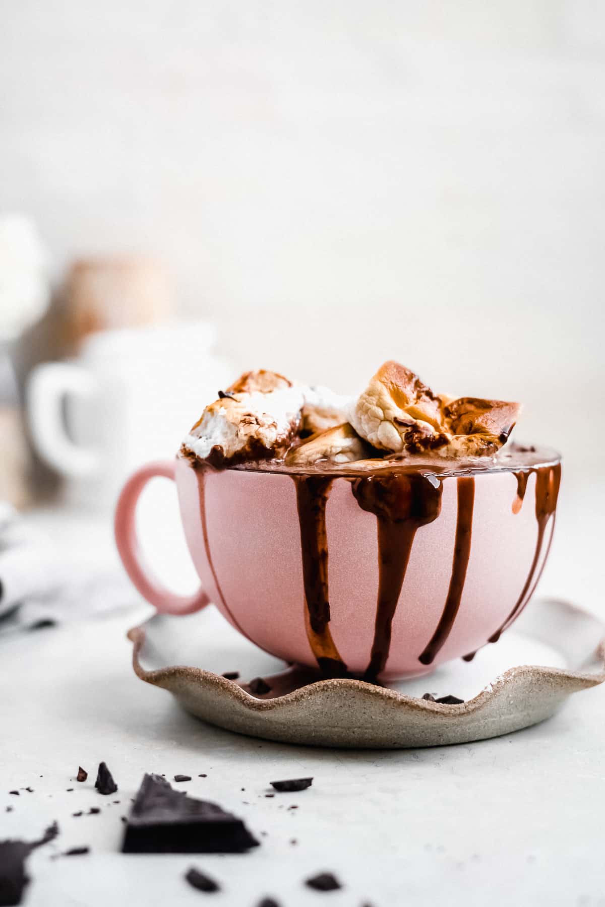 Side view of large pink mug sitting on top of a grey scalloped plate and filled to the brim with non dairy hot chocolate.