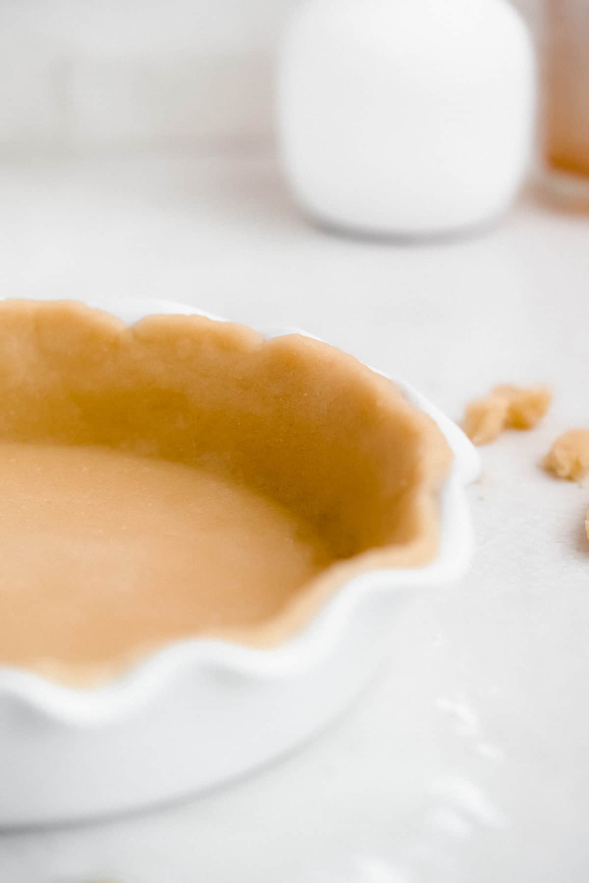 Close up view of the scalloped edge of the molded pie crust in the white ceramic pie crust pan.
