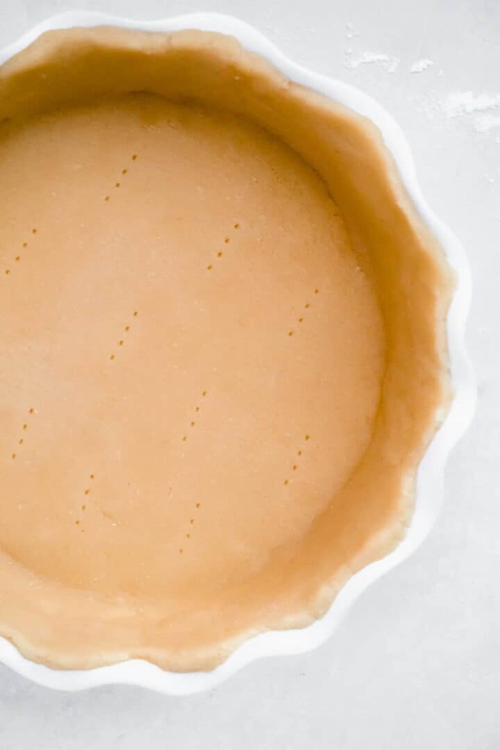 Close up overhead view of pie crust rolled and formed in the white scalloped pie crust pan. Fork pricks are made in the bottom of the pie crust.