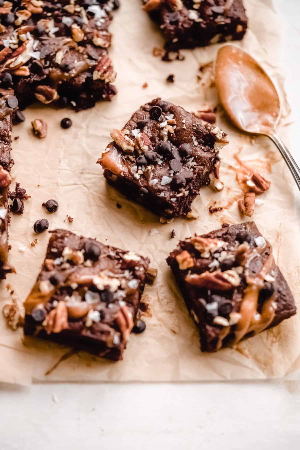Brownie squares on brown paper topped with nuts and caramel sauce.