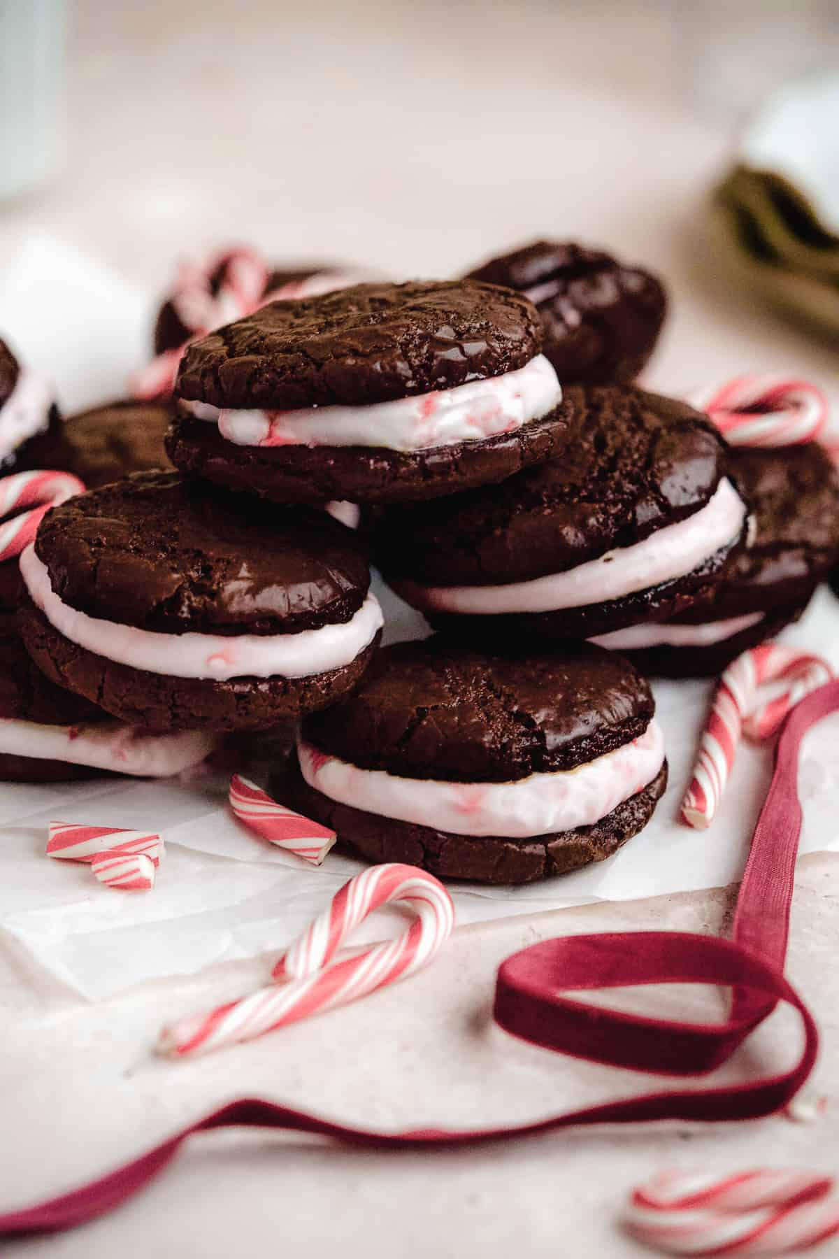 Close up side view of 6 Peppermint Brownie Sandwich Cookies mounded on white parchment paper.  