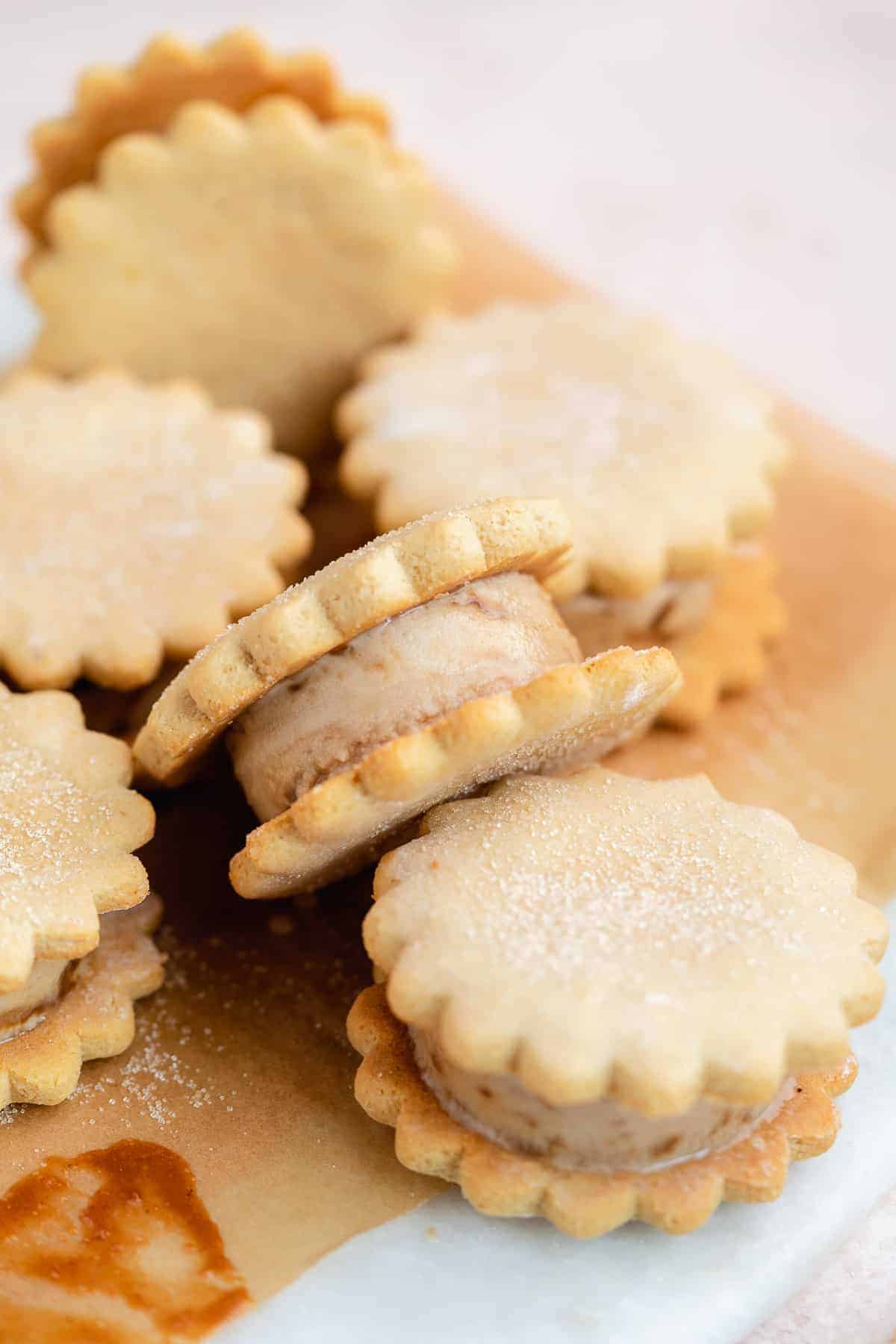 Six caramel sugar cookie ice cream sandwiches scattered on parchment paper to reveal top and side views of the delicious treat.