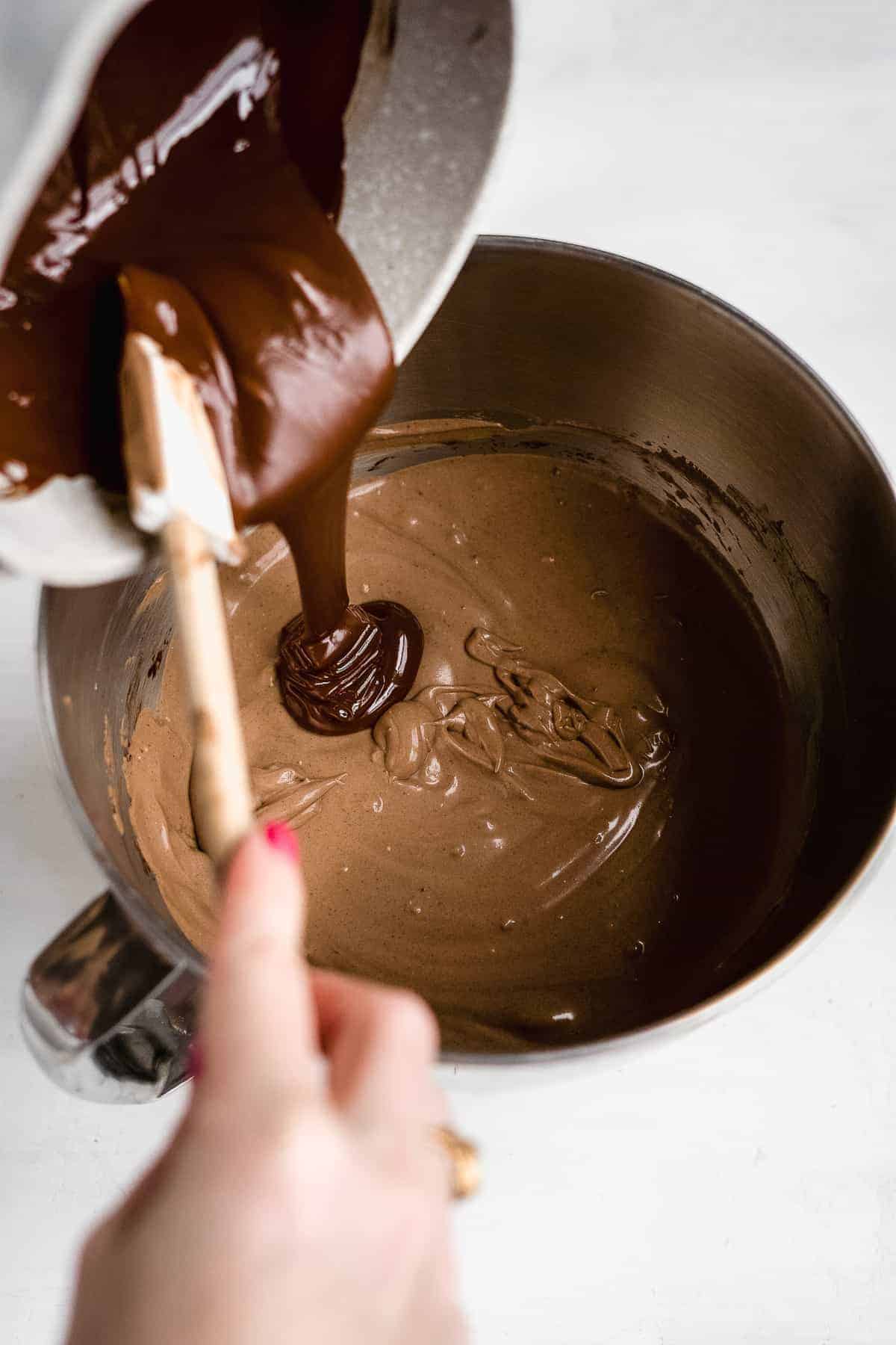 Melted chocolate being poured into a bowl with cheesecake batter.