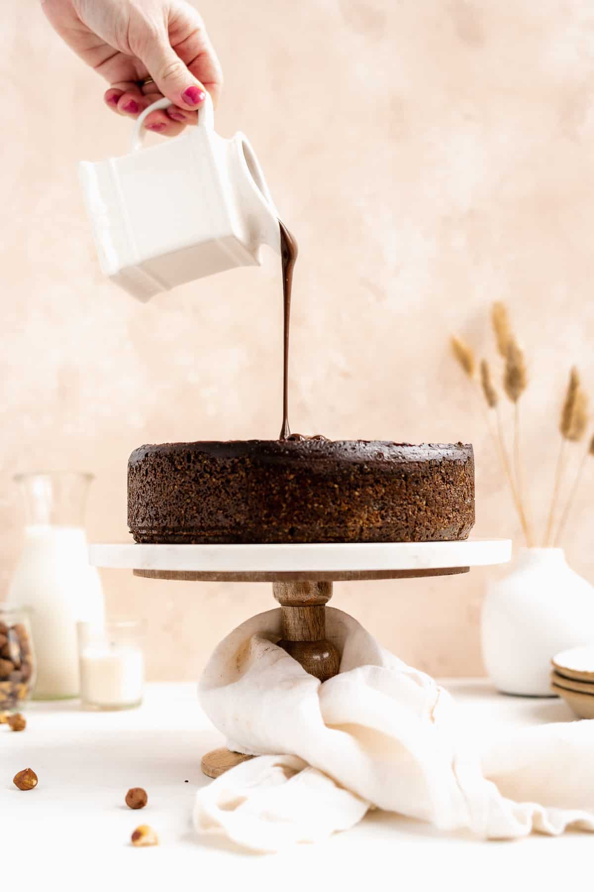 Side view of the chocolate ganache being poured over the top of the baked Chocolate Toasted Hazelnut Cheesecake.  