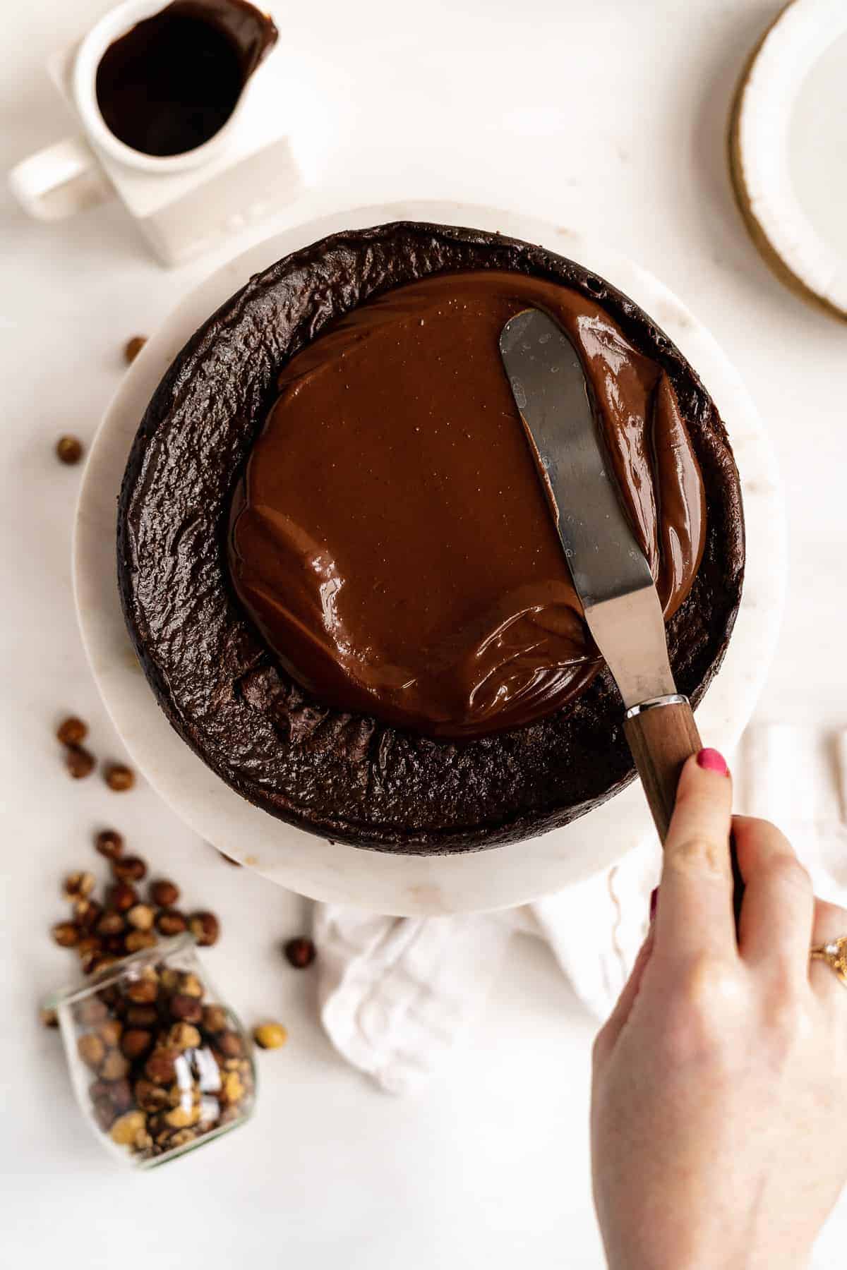 Person spreading chocolate ganache over baked cheesecake.