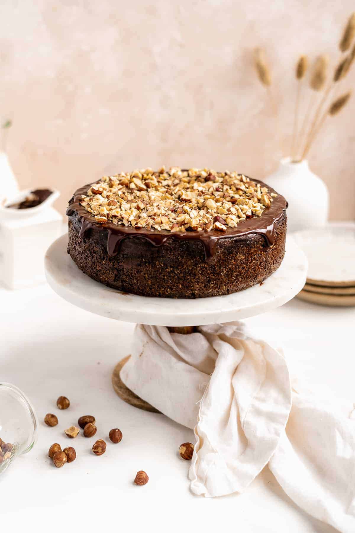 Side view of whole Chocolate Toasted Hazelnut Cheesecake sitting on top of a marble cake plate.  Hazelnut pieces are sprinkled around the base of the cake plate.  