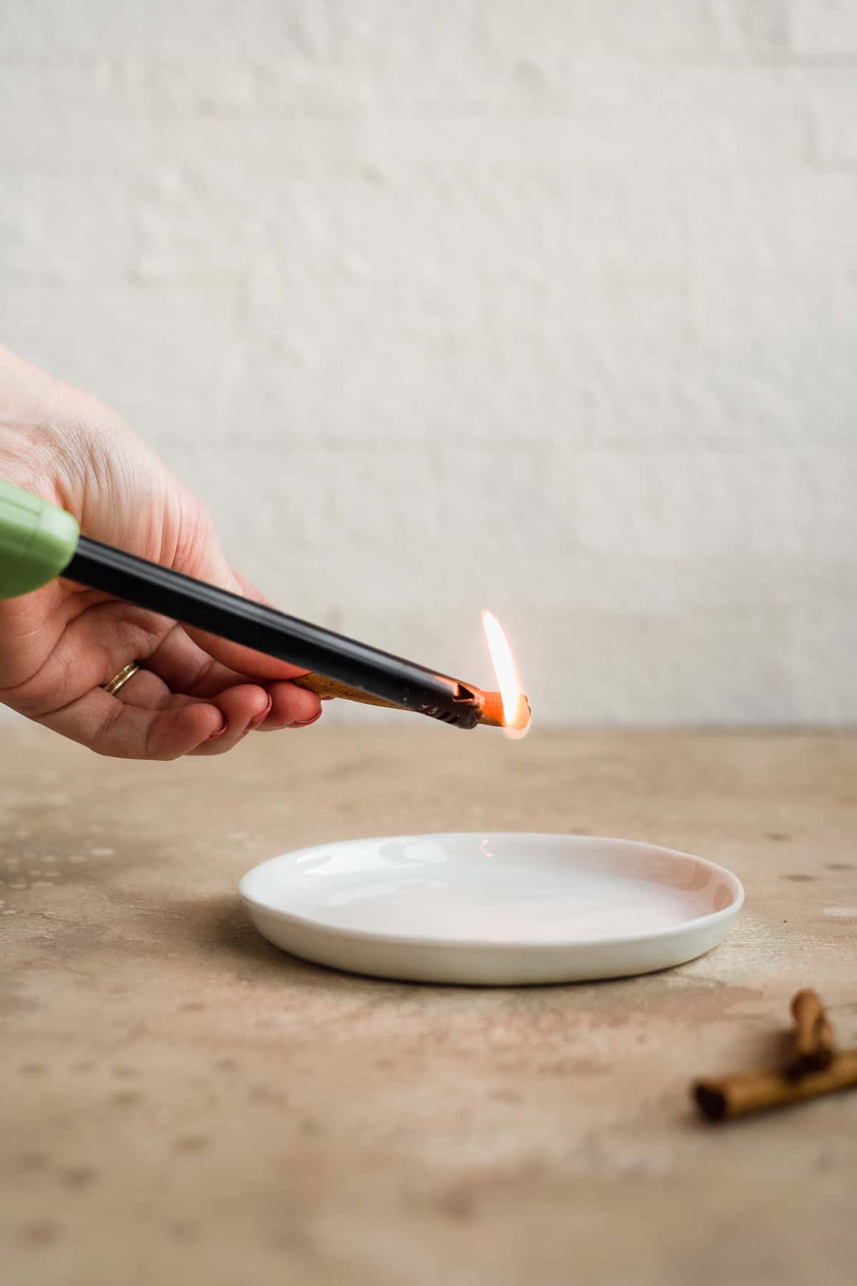 Person holding a lighter to a cinnamon stick over a white plate.