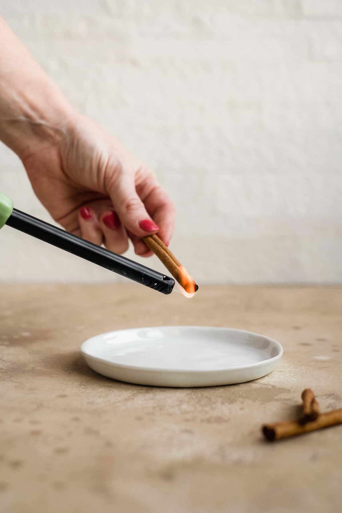 Person lighting a cinnamon stick on fire over a white plate.