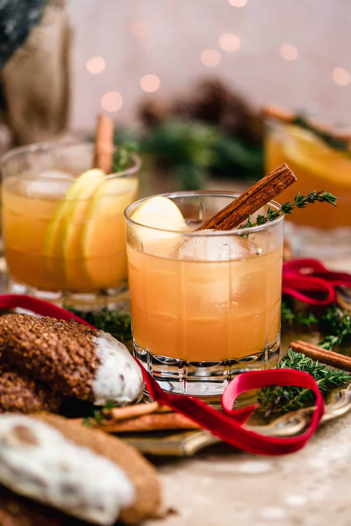 Side view of Smoked Cinnamon Apple Cider Bourbon Smash Cocktails in cut crystal glasses with assorted cookies nearby to enjoy!