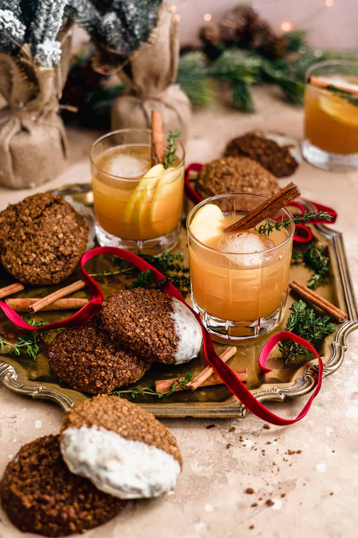 Two Smoked Cinnamon Apple Cider Bourbon Smash Cocktails in cut crystal glasses on a gold tray with cinnamon stick garnish and assorted cookies to enjoy while sipping!  