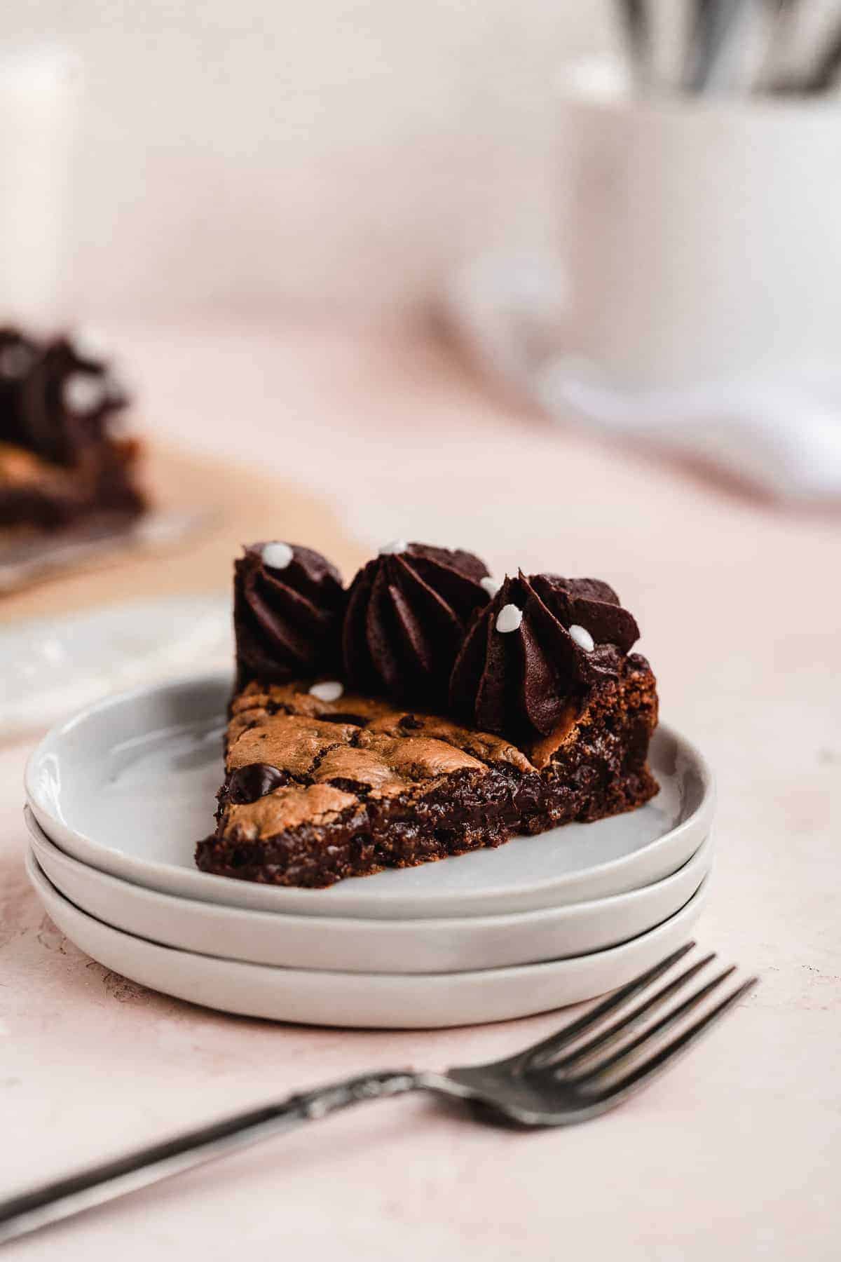 Stack of 3 dessert plates with one triangular piece of chocolate chip cookie cake sitting on top plate. Silver fork resting nearby.
