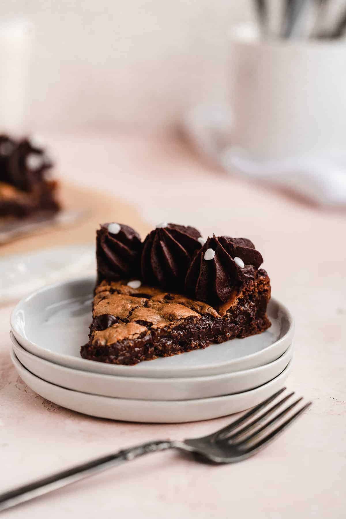 Stack of 3 dessert plates with one triangular piece of chocolate chip cookie cake sitting on top plate.  Silver fork resting nearby.  