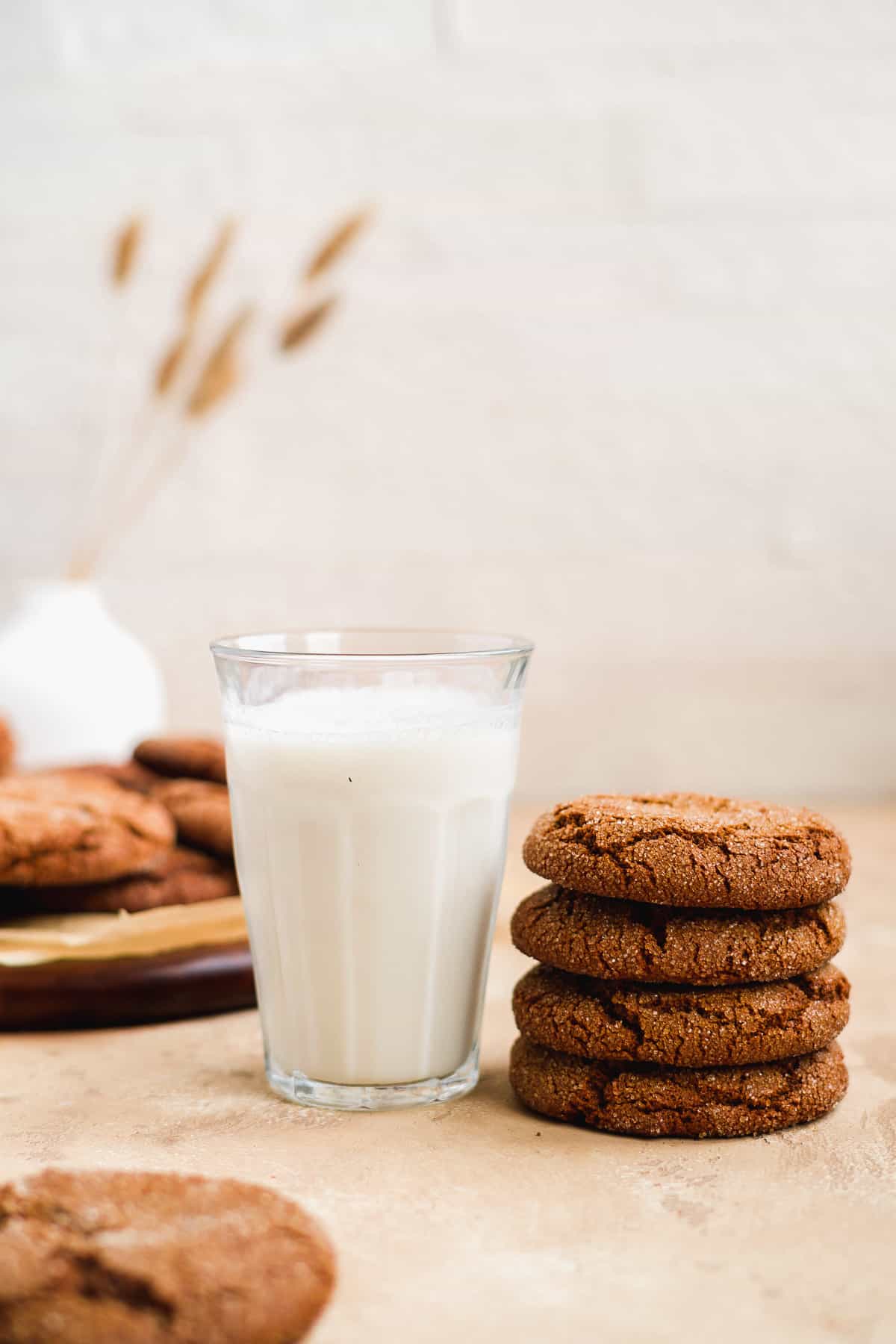 Side view of 4 stacked Soft and Chewy Ginger Snap Cookies sitting next to a cold glass of milk.  A plate of additional cookies is in the background.  