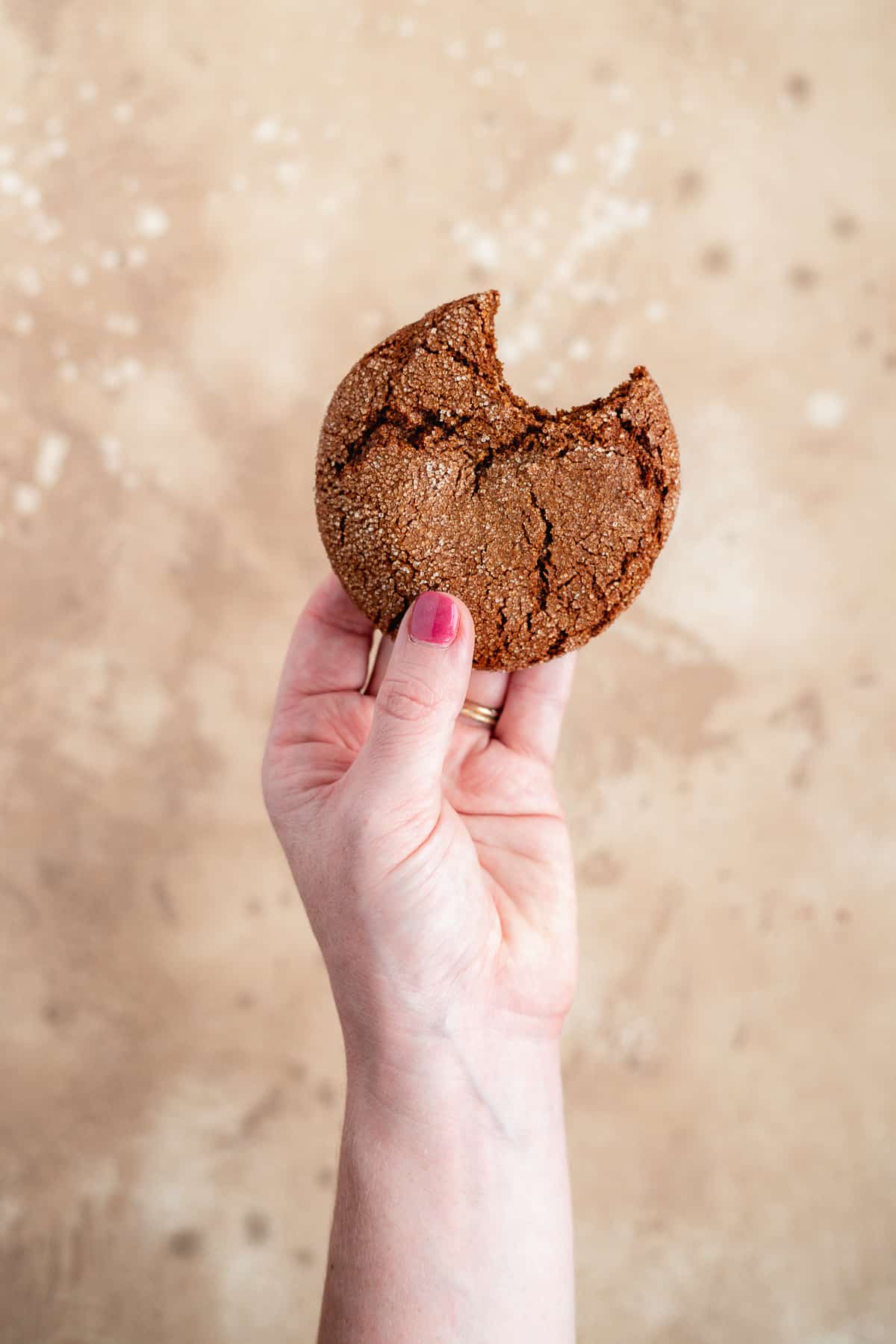 Side view of a single Soft and Chewy Ginger Snap Cookie with a bite taken out of it being held in a hand.  