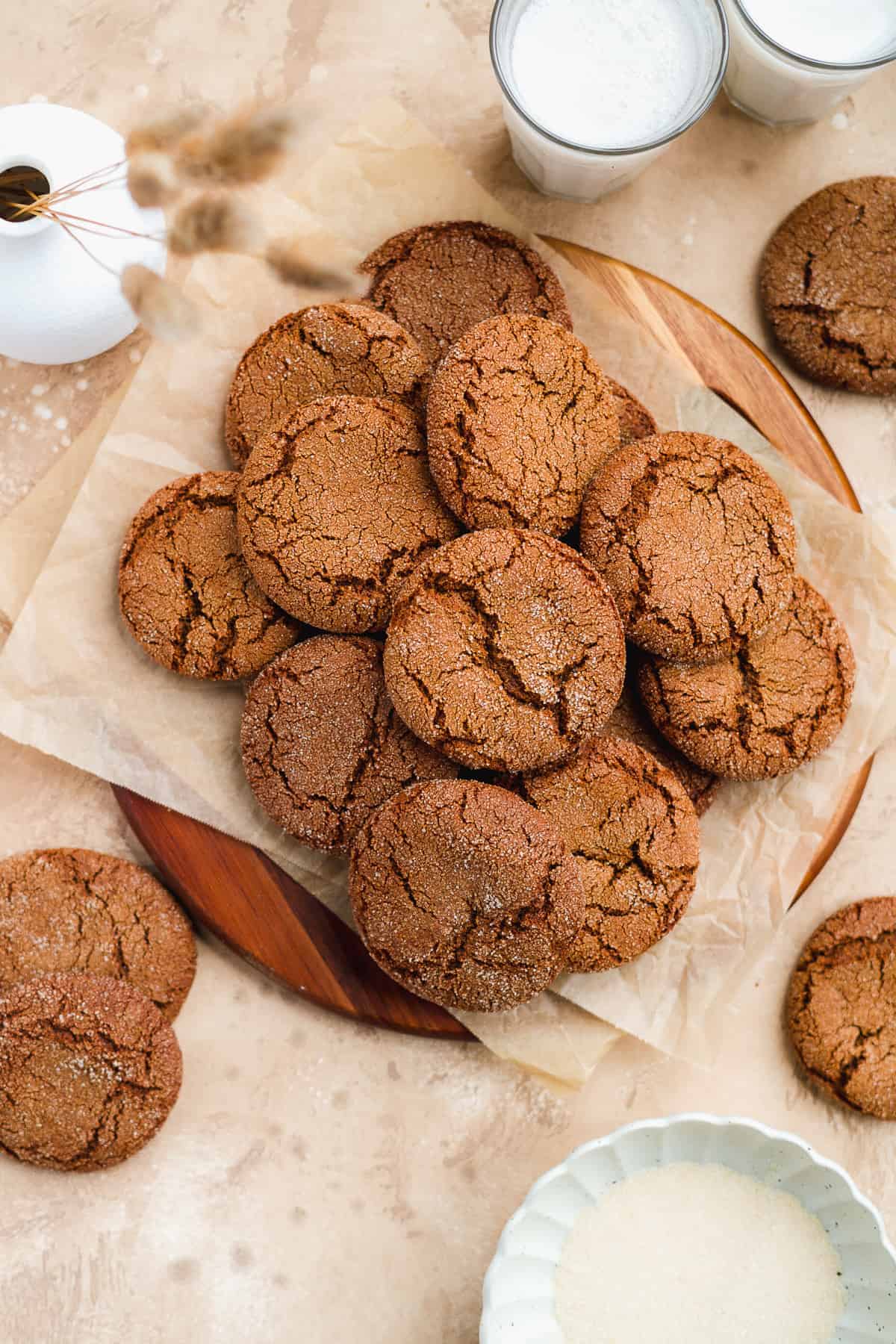 Overhead view of a dozen freshly baked Soft and Chewy Ginger Snap Cookies mounded on parchment paper on a wooden tray.