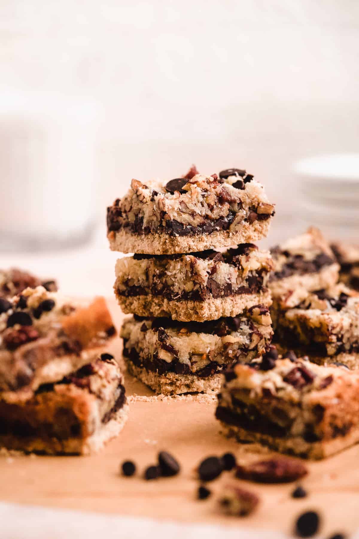 Side view of 3 Toasted Oat Seven Layer Magic Cookie Bars stacked on top of each other. Other cut bars are placed around the stack.
