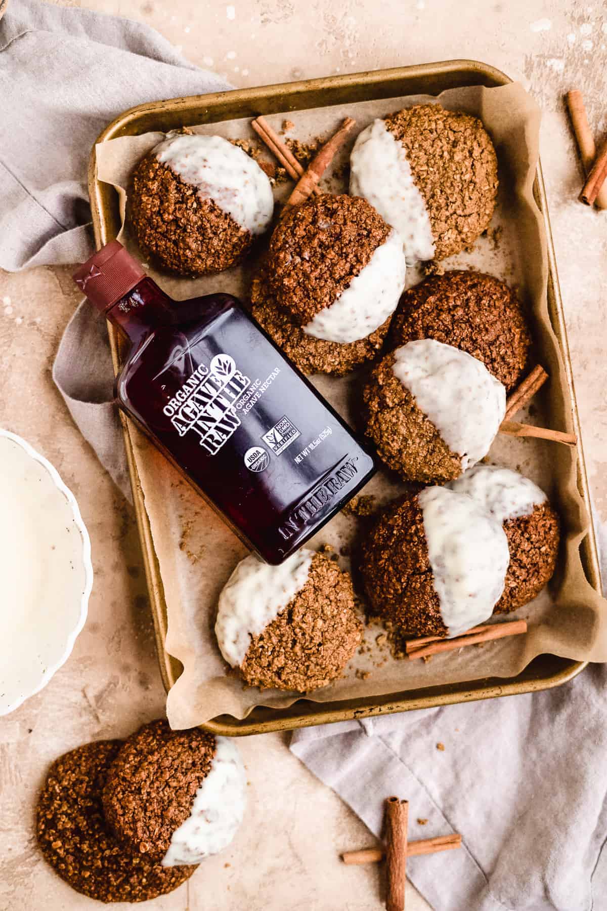 Gold baking sheet, parchment paper  with oatmeal gingerbread cookies dipped in white chocolate with bottle of In The Raw's Agave Nectar.  