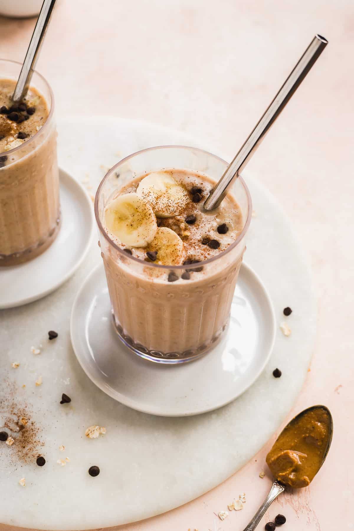 Cup filled with smoothie with toppings and a straw on a white plate.