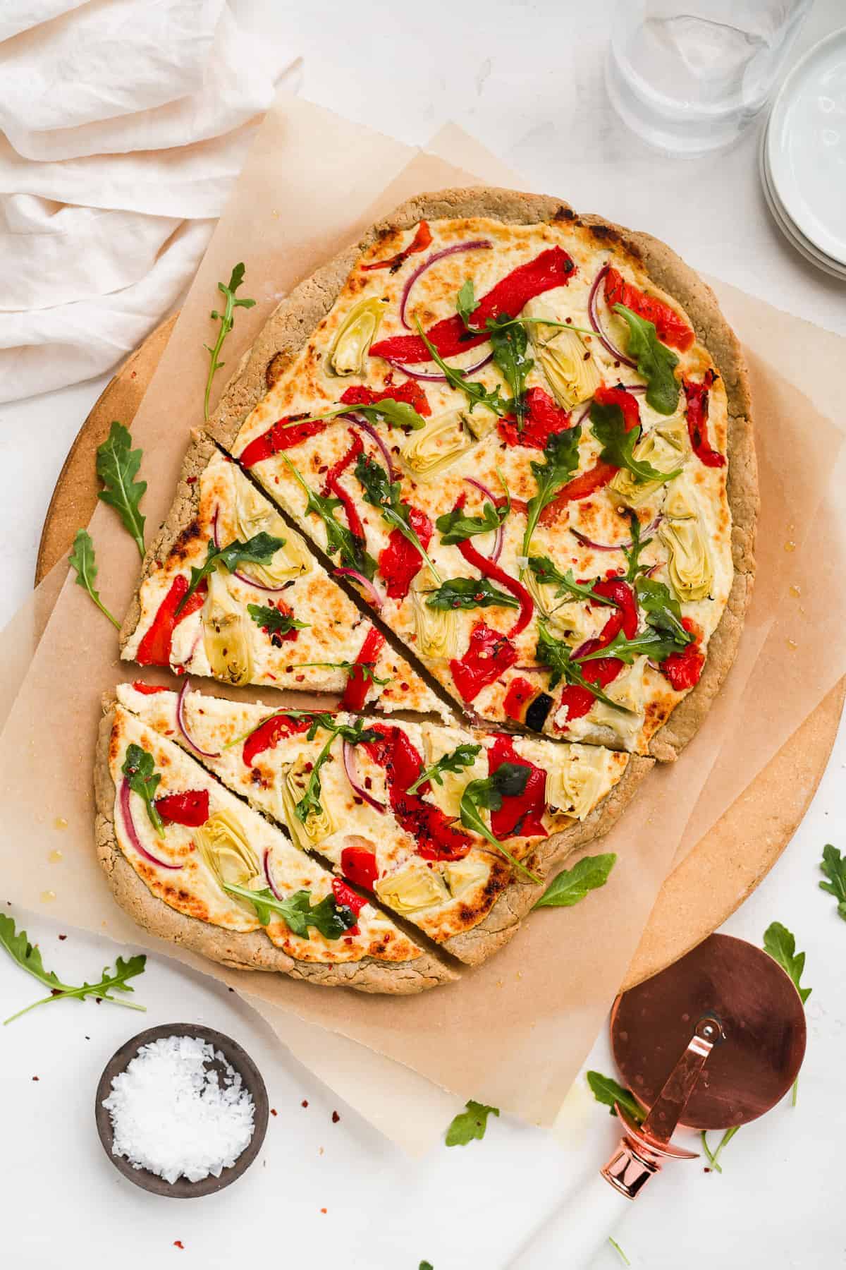 Baked pizza sliced on a brown pizza stone with red peppers and green herbs.