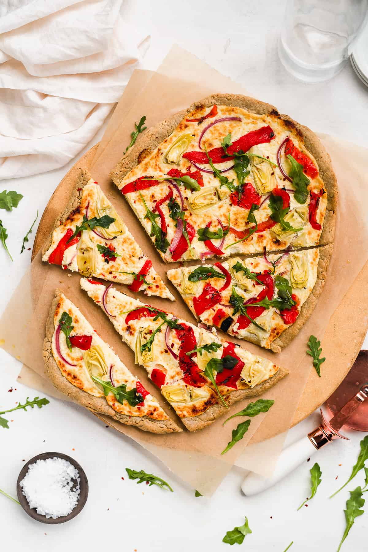 Sliced pizza on a pizza stone topped with red peppers and green herbs.