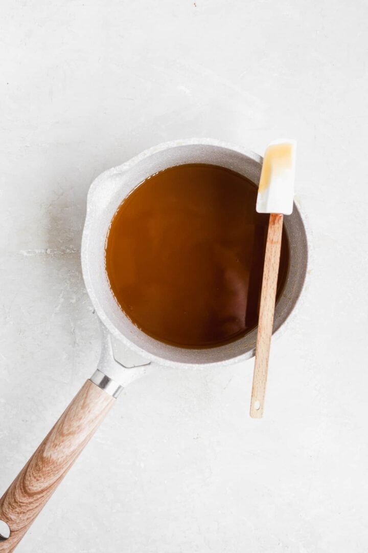 Gray pot with caramel inside on a white surface with a spatula resting on the edge of the pot.