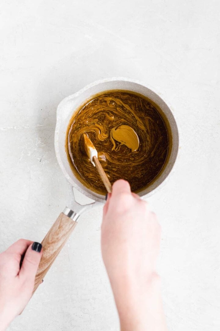 Hand mixing caramel sauce in a pot on a gray surface.