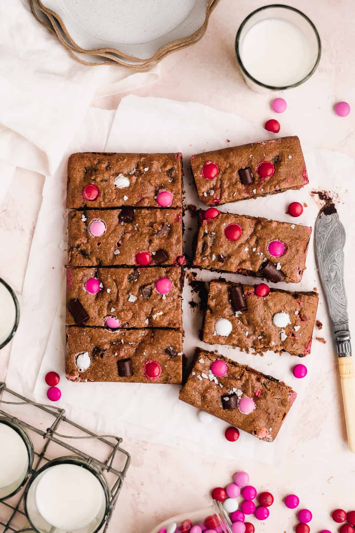 Cookies sliced into bars with red and pink M&Ms on top on white parchment paper.