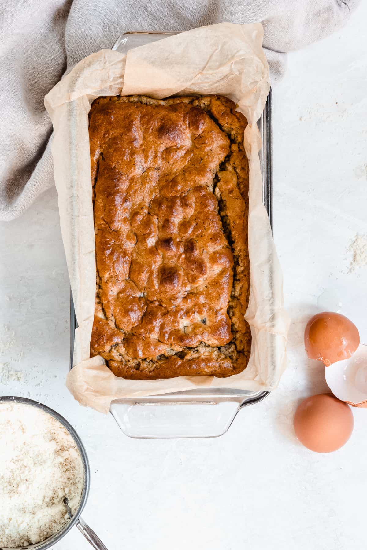 Overhead shot of banana bread in a loaf pan with egg shells and flour on the side.