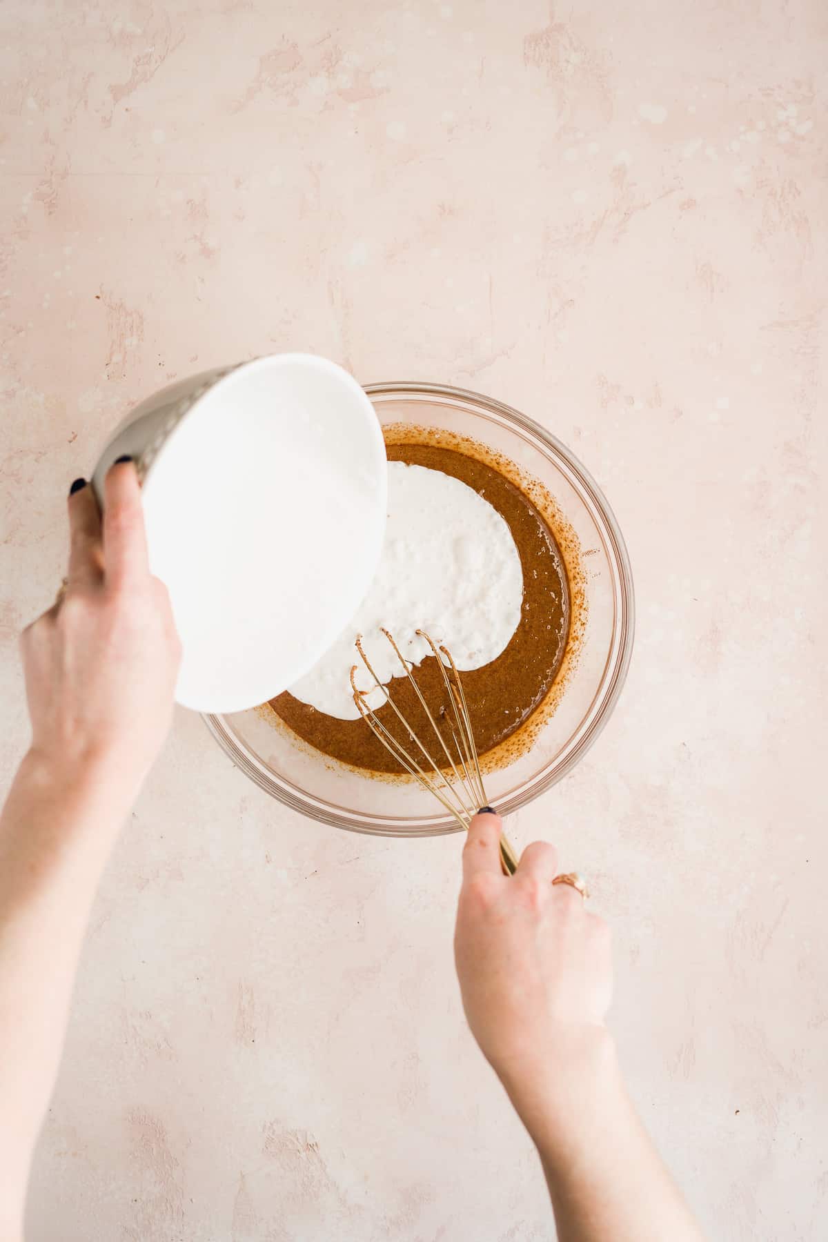 Person pouring coconut milk into a bowl with cake batter.