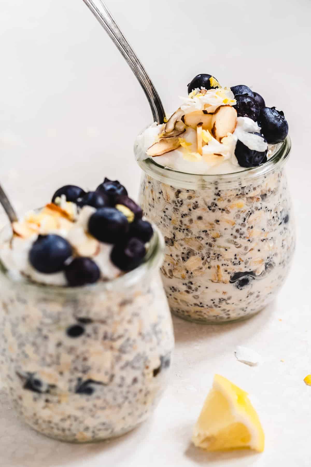 Two glass jars full of oats with blueberries and almonds on top.